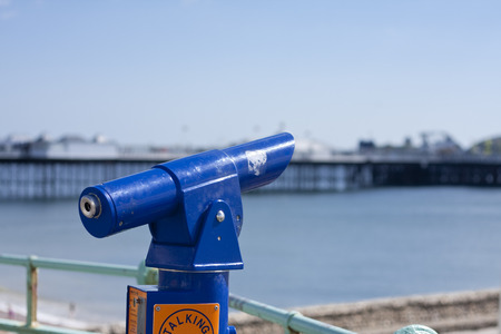 A blue sightseeing telescope looking out to sea with a pier in the backgroundの写真素材