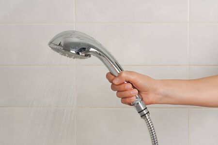 Hand holding the shower on backround of tiled  bath wallの写真素材