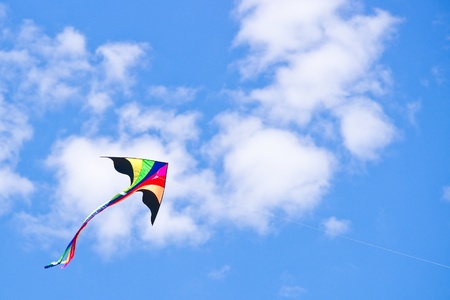 Multicolored kite flying in blue cloudy sky