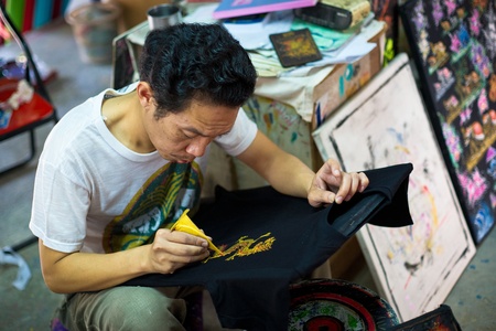 Bo Sang village, Chiang Mai province, Thailand - 9 January, 2012: Thai craftsman is drawing asian dragon on the souvenir t-shirt in Bo Sang handicrafts village. Any tourist can buy a blank t-shirt in the near placed store and the artist draws picture you のeditorial素材