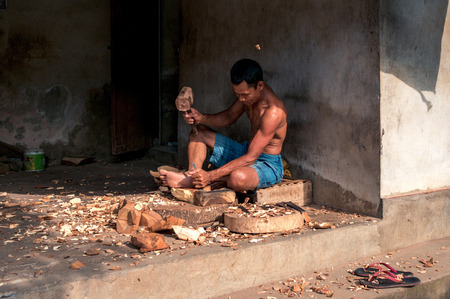 BALI, INDONESIA - OCTOBER 31, 2016: Balinese carpenter is working in his workshop placed in Tirta Tawar street in Ubud, Bali, Indonesia. He is sitting on the floor and carving from the wood by the hammer and special knife.のeditorial素材
