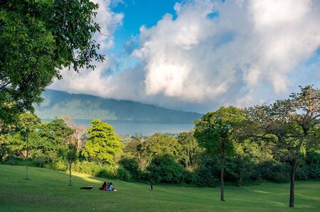 BALI, INDONESIA - OCTOBER 13, 2016: Group of people are relaxing on the meadow of botanical garden with great view on Bratan lakeのeditorial素材