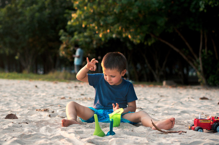 Little boy sitting on the sand and playing with plastic toys on Nopharatthara beach, Krabi province, Thailandの写真素材