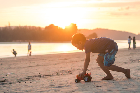 Little boy playing with plastic truck on Nopharatthara beach at sunset, Krabi province, Thailandの写真素材