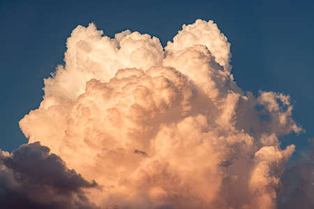 Giant cumulus cloud in the sunset orange sun raysの写真素材