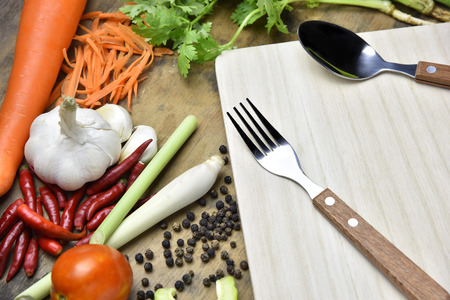 Spoon and fork with vegetables on wooden background