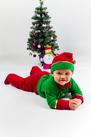 Baby boy dressed as Santa's Helper lying next to Christmas tree. の写真素材