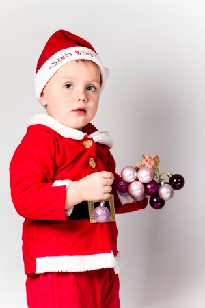 Baby boy dressed as Santa Claus holding Christmas baubles. White background.の写真素材