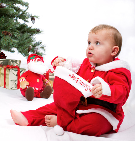 Santa Baby boy sitting next to Christmas tree. Studio shoot on white .の写真素材