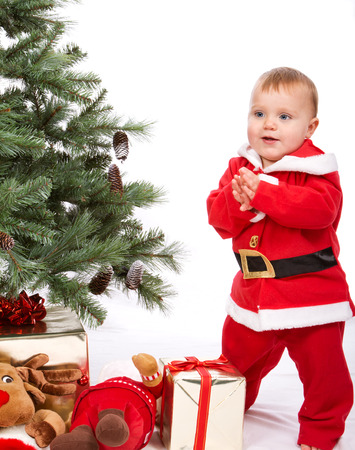 Santa Baby boy standing next to Christmas tree. Studio shoot on white .の写真素材