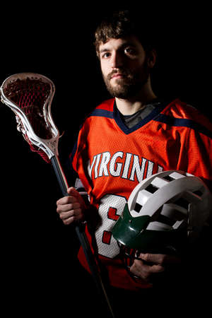 Lacrosse player holding helmet and stick. Studio shoot on the black .の写真素材