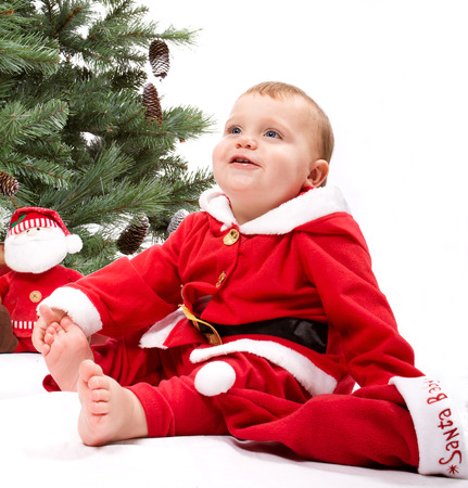 Santa Baby boy sitting next to Christmas tree. Studio shoot on white .の写真素材
