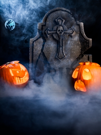 Angry face and scared face of Halloween pumpkins with moon, tombstone and bat on misty dark background.の写真素材