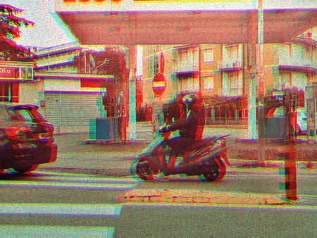 Photography of a scooterist passing a gas station on a scooter.の写真素材