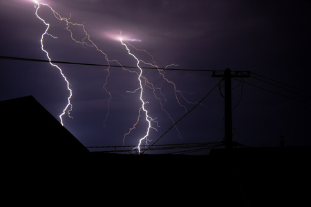 Bright lighting in the night sky with a house and power line pole on foregrown