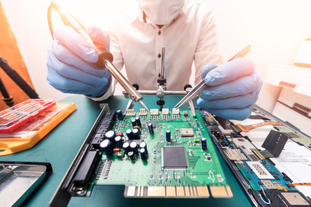 The asian technician repairing the motherboard by soldering in the lab. the concept of computer hardware, mobile phone, electronic, repairing, upgrade and technology.