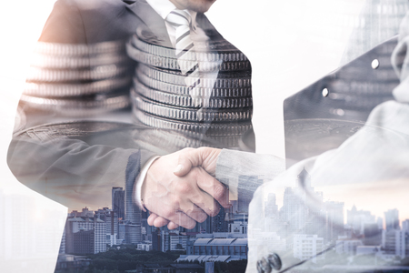 The double exposure image of the businessman handshaking with another one during sunrise overlay with cityscape and coin stack image. The concept of modern life, business, city life and partnership.の写真素材
