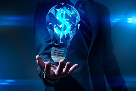 The abstract image of the hand holds the illumination lamp and the dollar sign inside. the concept of financial, idea, futuristic, business and technology.の写真素材