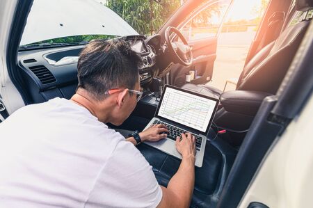 The asian technician analyze the car's engine graph on laptop computer in the garage. the concept of...