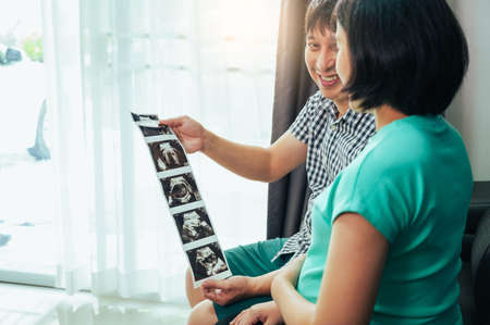 Asian woman and her son are looking at an ultrasound image of their baby.