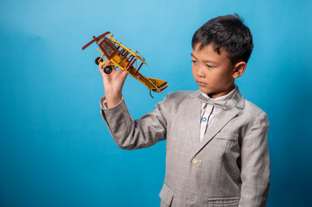 the studio shot isolated image of the boy playing the miniture airplane with the blue backdropの写真素材