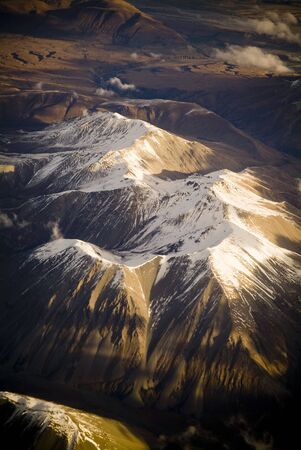 Aerial view of mountain range with snow capped peaks in late afternoon lightの写真素材
