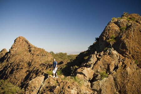 A man walks along the ridgline of red and orange coloured mountains in Mt Kaputar National Park, Australia.の写真素材
