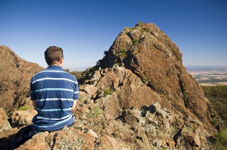 Hiker pauses for a break sitting on a ledge overlooking the ridge aheadの写真素材