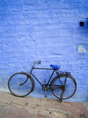 Old bike leans up against a bright blue brick wallの写真素材