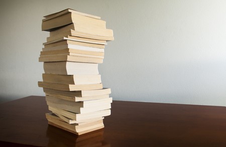 A large pile of books sits on a timber desktop with blank space behindの写真素材