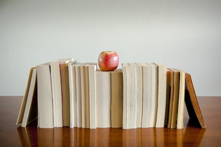 A row of books with an apple on top sits on a timber table with blank space behindの写真素材