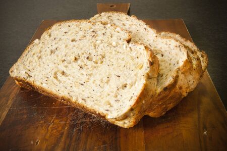Wide slices of bread with mixed grains on a timber bread boardの写真素材
