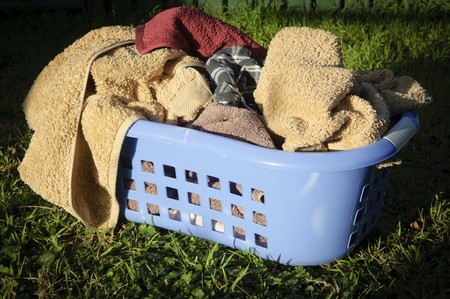 Blue laundry basket filled with towels sits on a lawn outsideの写真素材