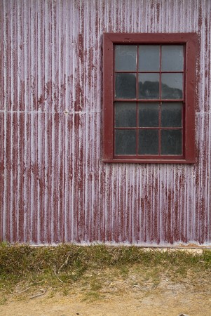 Red tin wall with a window and sandy groundの写真素材