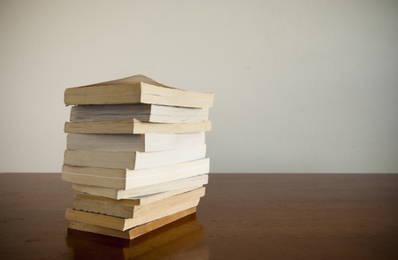 A large pile of books sits on a timber desktop with blank space behindの写真素材