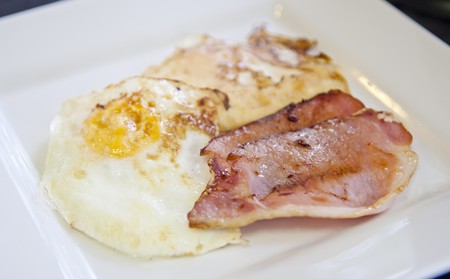 Homemade breakfast of bacon and eggs in white square plateの写真素材