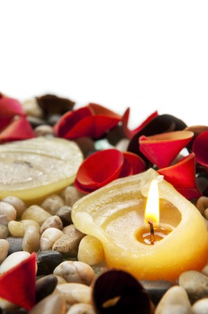 A burning candle amongst small stones and bright petalsの写真素材