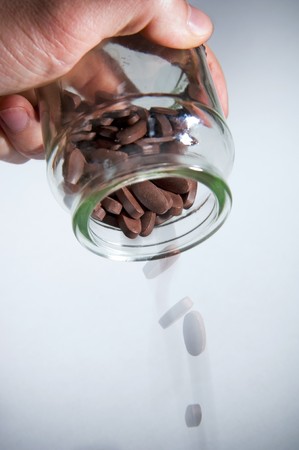 Large brown pills are poured out of a glass bottle with motion blurの写真素材
