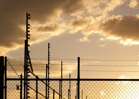 Large fences and barbed wire against a sunset sky with copy spaceの写真素材