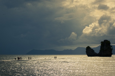 Silhouetted people seemingly walking on water leading to an islandの写真素材