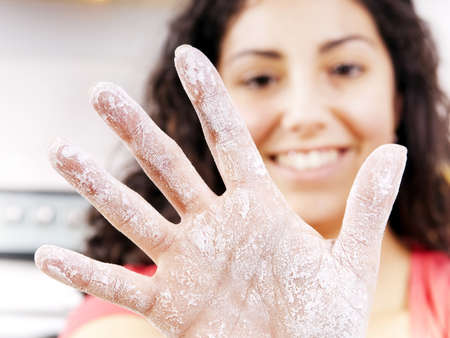 A smiling woman holds out a hand covered in flour while cookingの写真素材