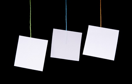 Multiple white paper tags hang on colorful string over blackの写真素材
