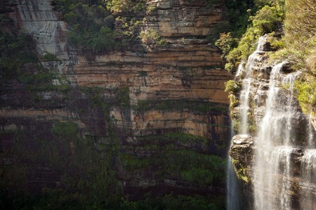 Waterfall in bright sun with darkened cliffs behindの写真素材