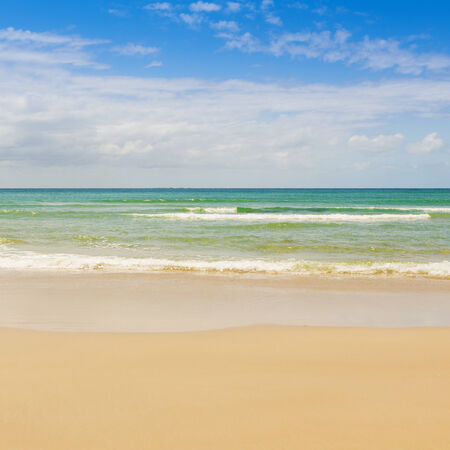 Beach with blue sky and blue water lapping the sandの写真素材