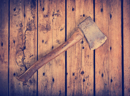 An old axe with a wooden handle and wear marks sits on a rough timber background filteredの写真素材