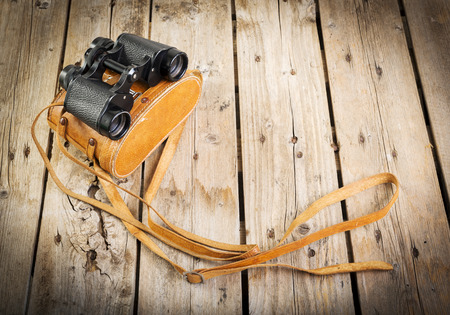 Pair of old binoculars with vintage leather strap and case on a rough wooden surfaceの写真素材