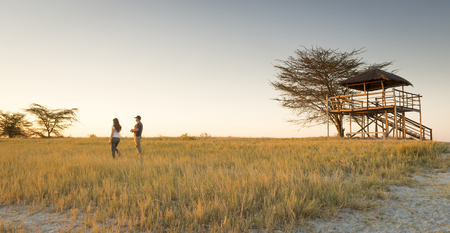 A young couple stand in long grass and watch the sunset while on safari in the Makgadikgadi Pans, Botswana, Africaの写真素材