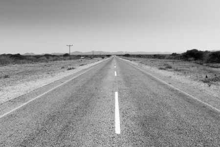 Road in Botswana, Africa stretching off into the distance under a blue sky in black and whiteの写真素材