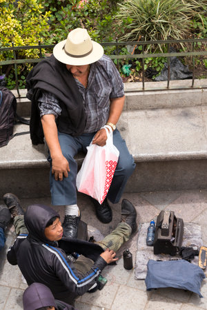 SAN JUAN OSTUNCALCO, GUATEMALA - JUNE 24: An unidentified man on a park bench gets shoe shined by an unidentified child at the San Juan Ostuncalco central park on June 24, 2017 in Guatemala.のeditorial素材