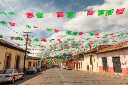 SAN CRISTOBAL, MEXICO - NOVEMBER 27: Unidentified people on a quiet street lined with colorful paper flags or papel picado in the Mexican flag colors on November 27, 2016 in San Cristobal. Papel picado flags are considered a folk art in Mexico.のeditorial素材